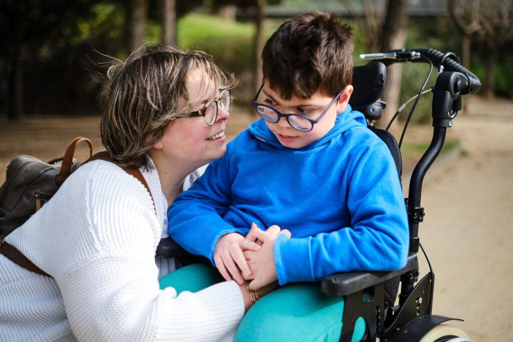 Disabled boy in a wheelchair enjoying a walk outdoors with his mother. Disability concept.